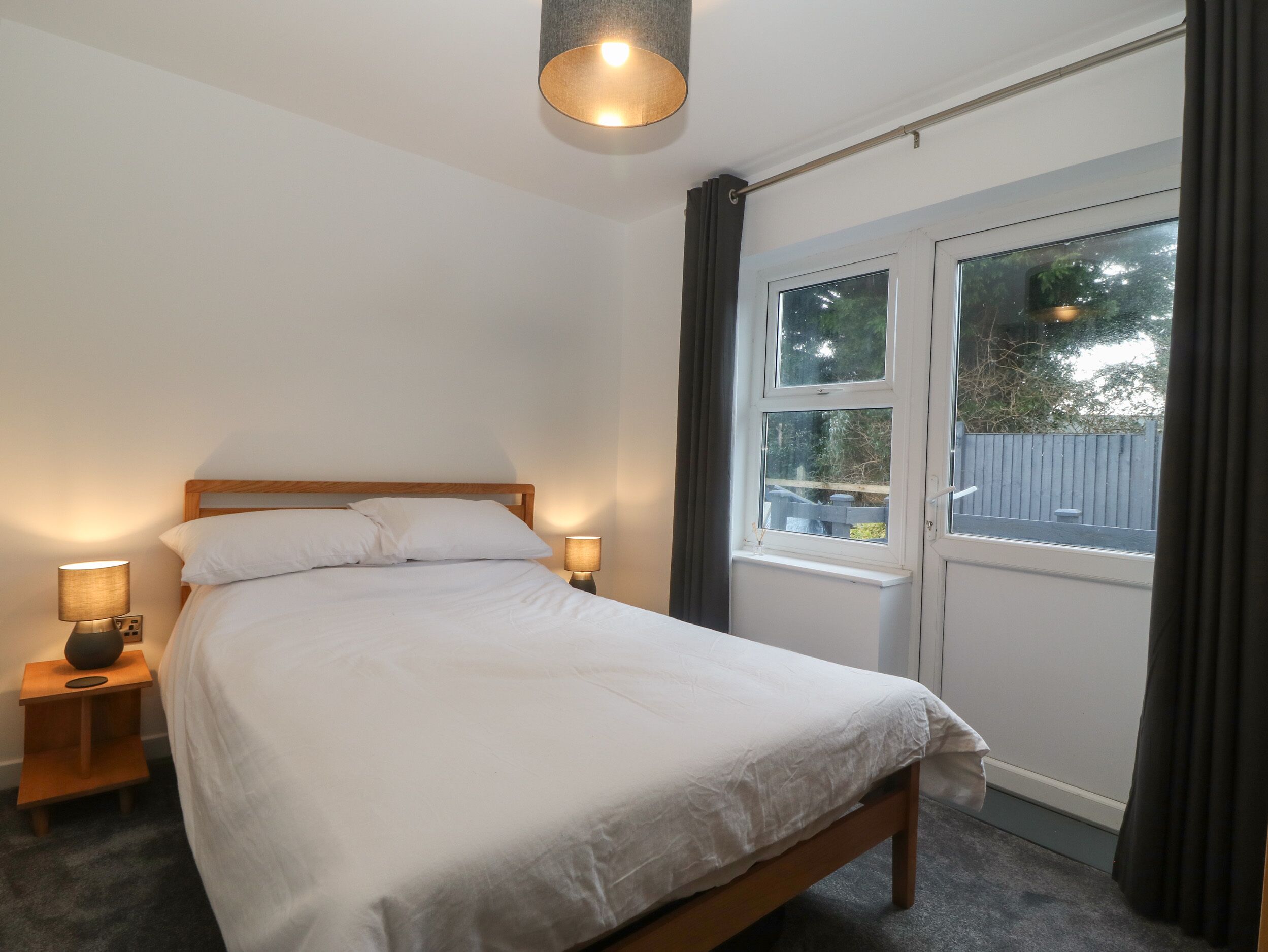 Een slaapkamer met een bed, twee bedlampjes, een raam met gordijnen en een plafondlamp.