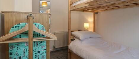 A bunk bed room with a wooden headboard, a hanging rack with patterned fabric, a bedside lamp, and a radiator.