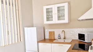 Una cocina moderna con piso de madera, gabinetes blancos, microondas integrado y una ventana con persianas verticales.