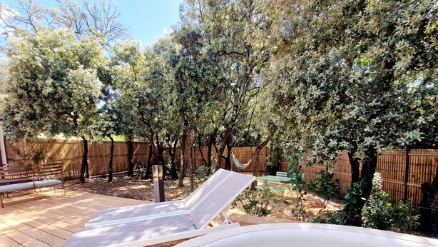 Un patio trasero con un jacuzzi, una terraza de madera y una hamaca.