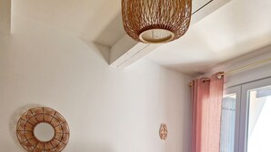 Una sala moderna con un televisor de pantalla plana sobre un mueble de madera, una mesa blanca y un ventanal con cortinas rosadas.