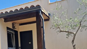 Un edificio con un porche de madera, una puerta negra y un pequeño árbol.