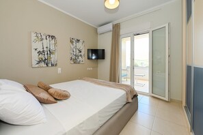Habitación de hotel con una cama, dos cuadros, un televisor y una puerta corrediza de vidrio a un balcón.
