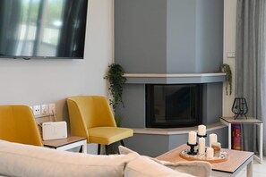 Una sala moderna con chimenea, un sofá, un sillón amarillo, una mesa de centro con velas y un televisor de pantalla plana montado en la pared.