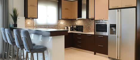 A modern kitchen with a central island, bar stools, a refrigerator, and a coffee machine.