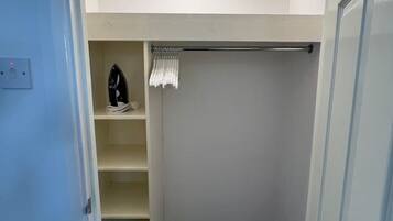 Een inloopkast met een kledingroede, planken en een klein strijkplank.