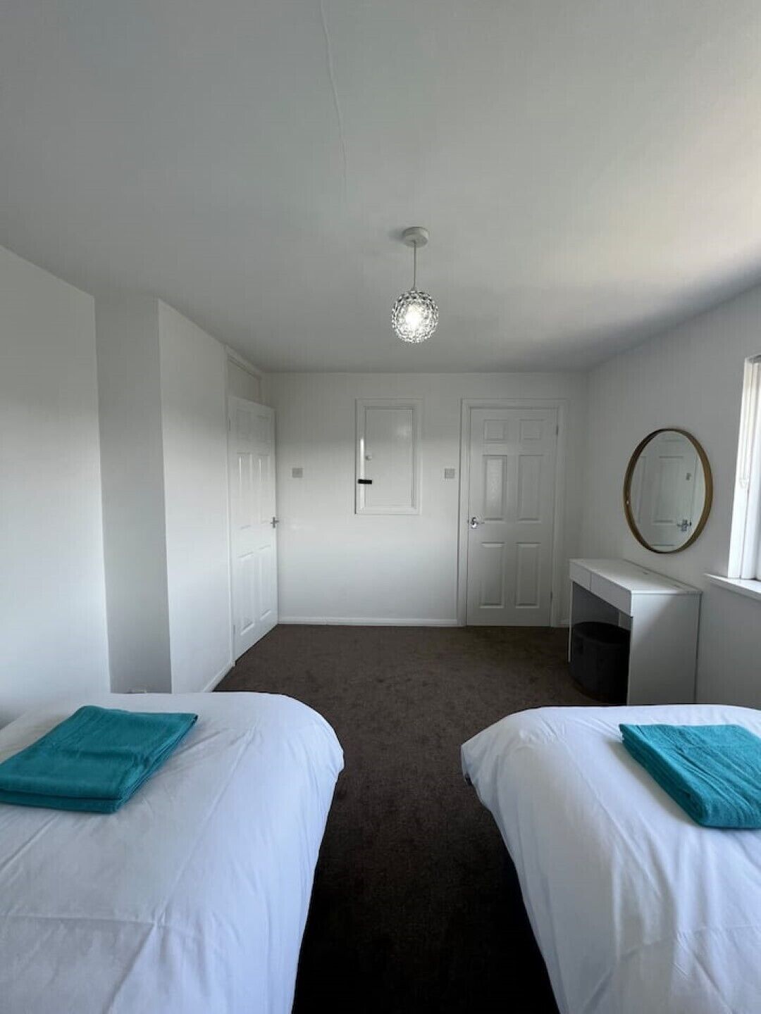 A bedroom with two beds, a desk, a mirror, and a ceiling light.