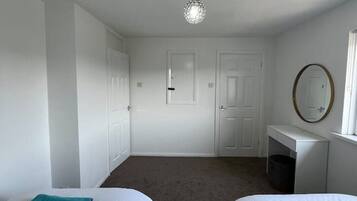 A bedroom with two beds, a desk, a mirror, and a ceiling light.