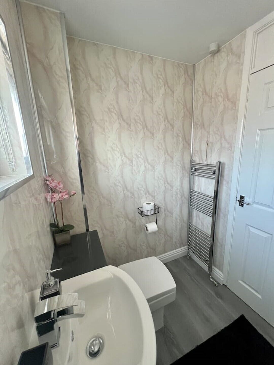 Een moderne badkamer met een witte wasbak, wanden met een marmerprint, een handdoekhouder en een toiletrolhouder.