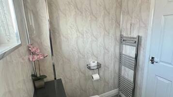 Een moderne badkamer met een witte wasbak, wanden met een marmerprint, een handdoekhouder en een toiletrolhouder.