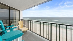 Un balcon avec deux chaises et une table, donnant sur une plage où l’on peut admirer les vagues.
