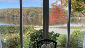 Vista desde una habitación con un ventanal grande que da a un lago, rodeado de follaje otoñal.