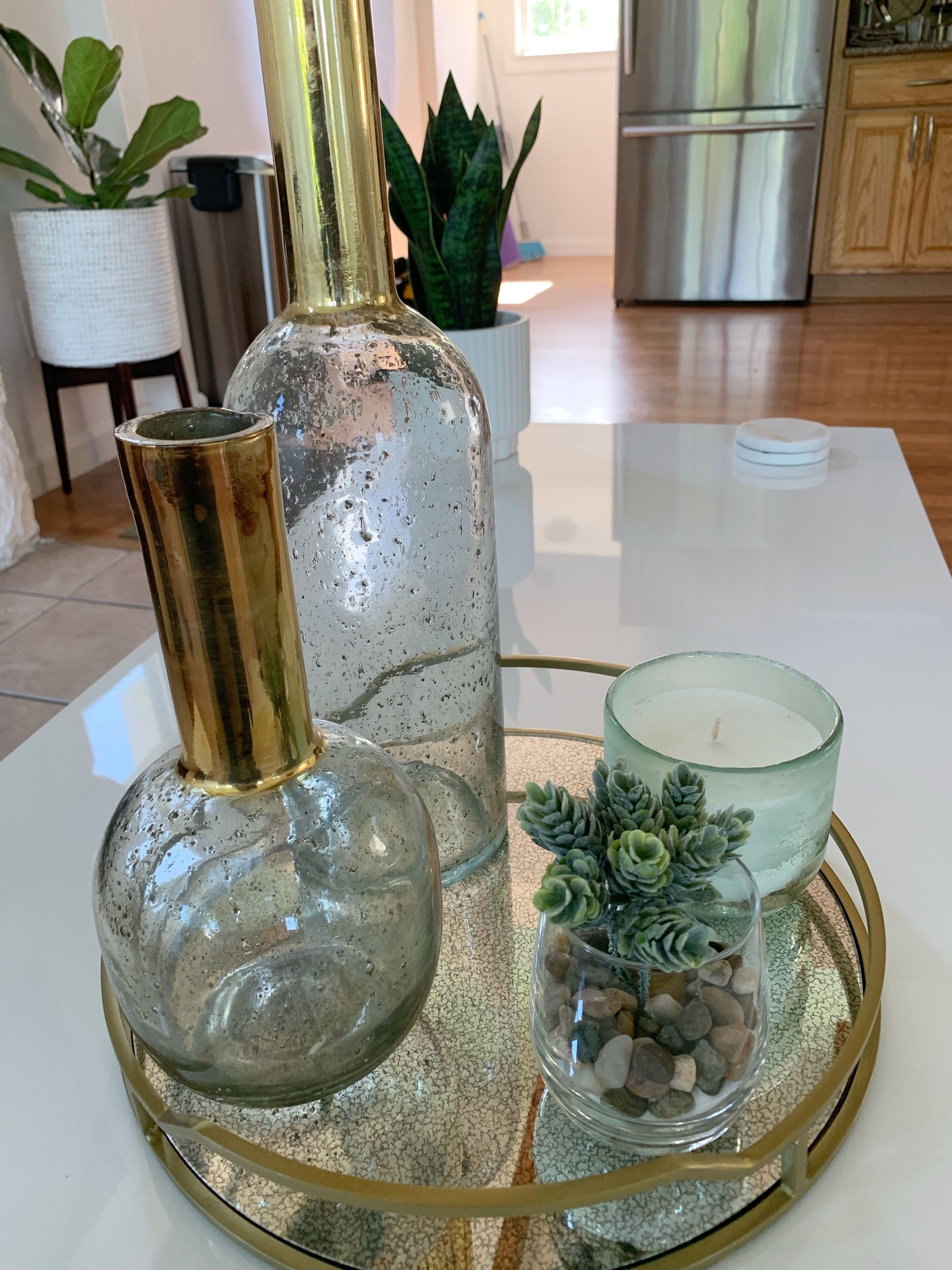 Une table en verre avec un plateau doré, un vase en verre transparent, un chandelier en verre et une petite plante succulente.