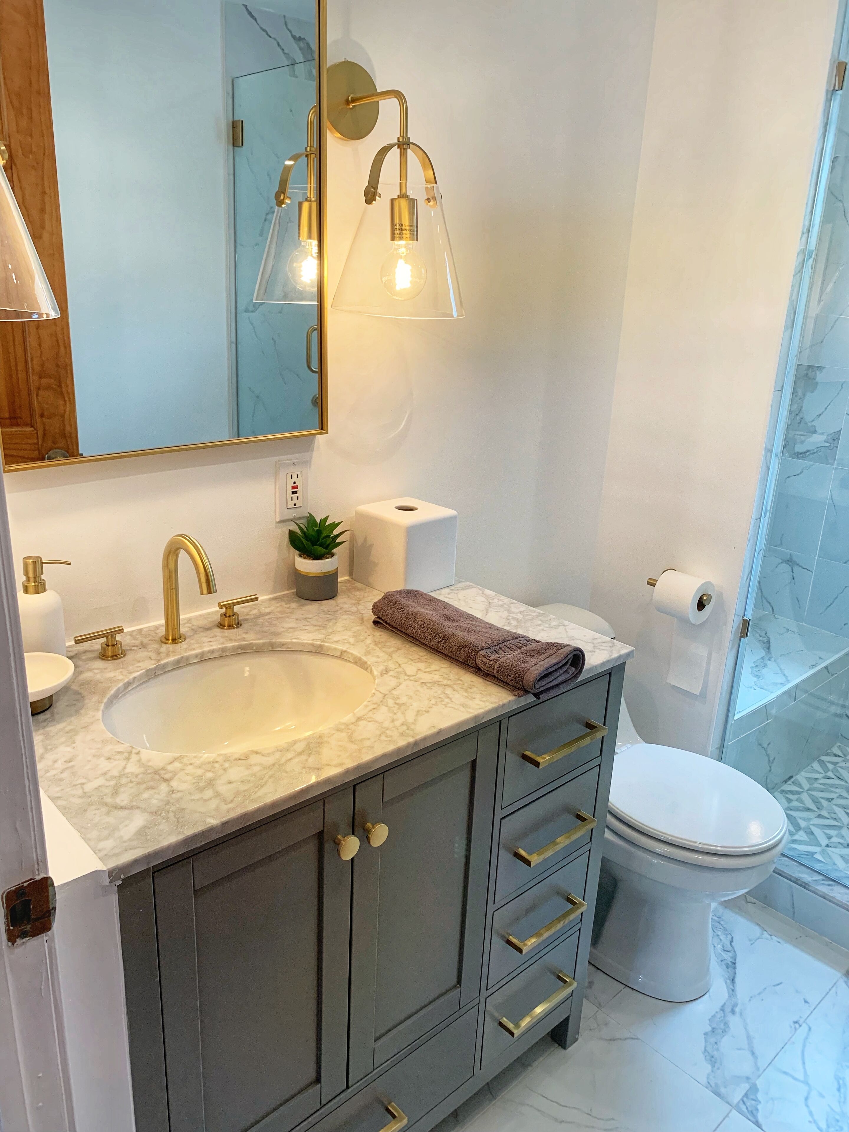 Un baño con lavamanos de mármol, accesorios dorados, un espejo y un inodoro.