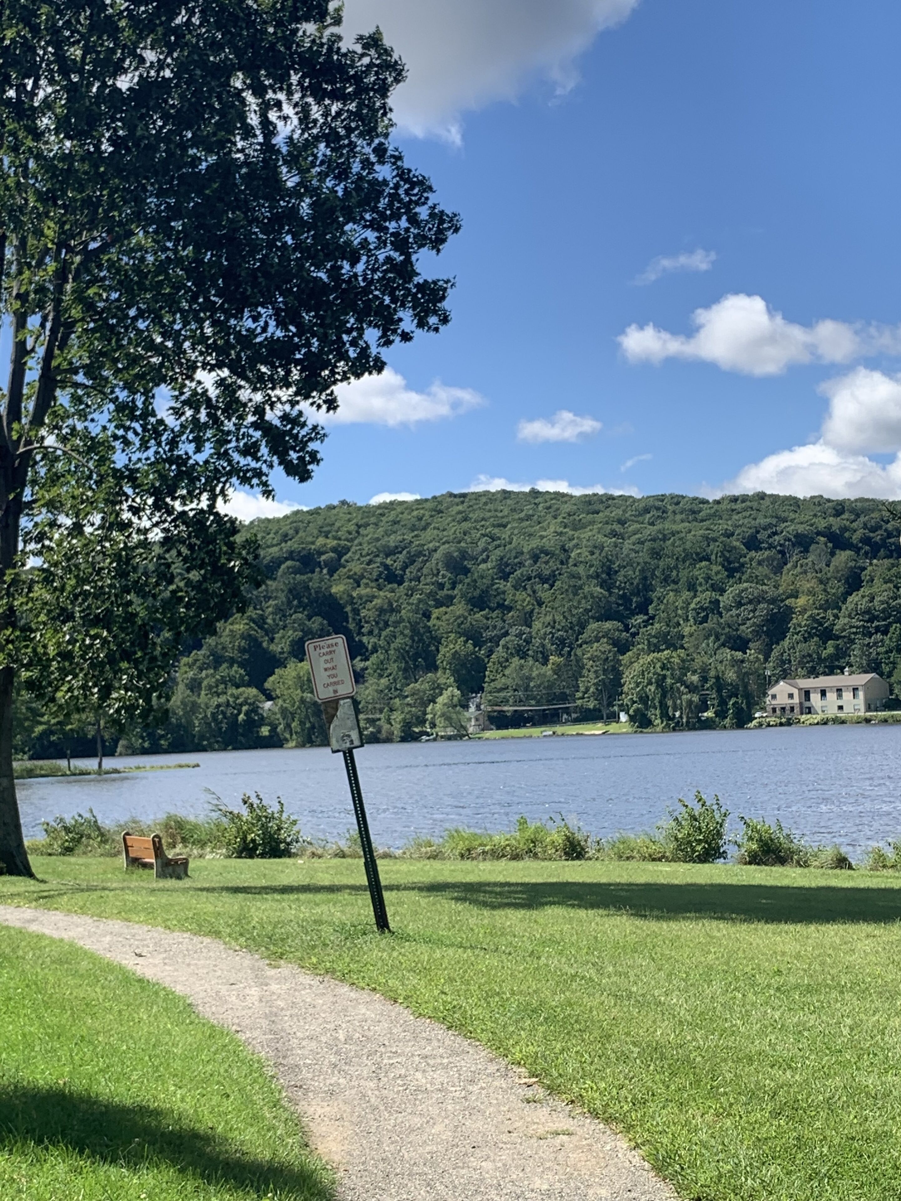 A lakeside path with a bench, a sign, and a house in the background.