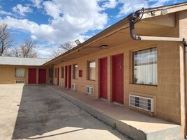 Filas de habitaciones de motel de un piso, con puertas y ventanas rojas, un área exterior cubierta y cielo despejado.