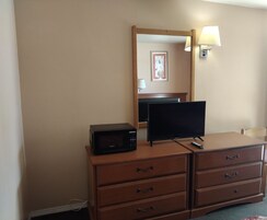 Habitación de hotel con tocador de madera, televisor de pantalla plana, microondas, lámpara y un cuadro en la pared.