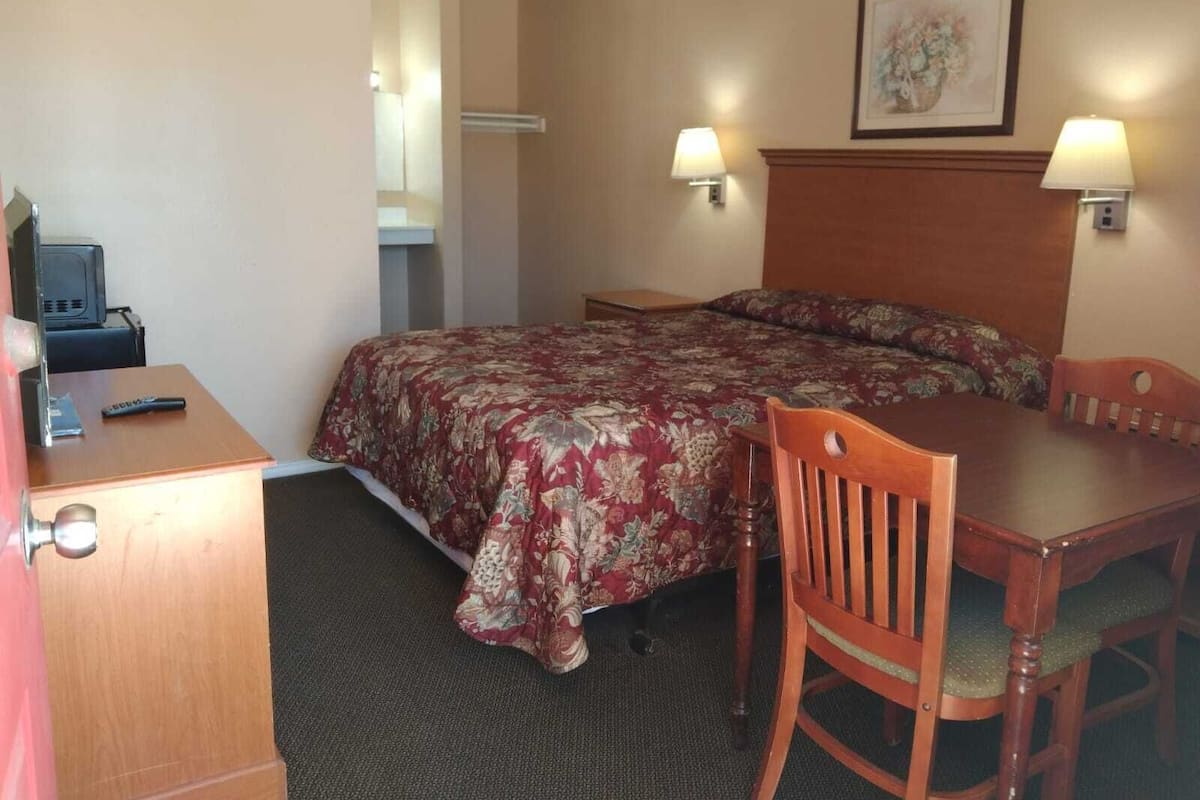 Ein Hotelzimmer mit einem Bett, einem Schreibtisch, einem Sessel, einem Fernseher und zwei Wandleuchten.