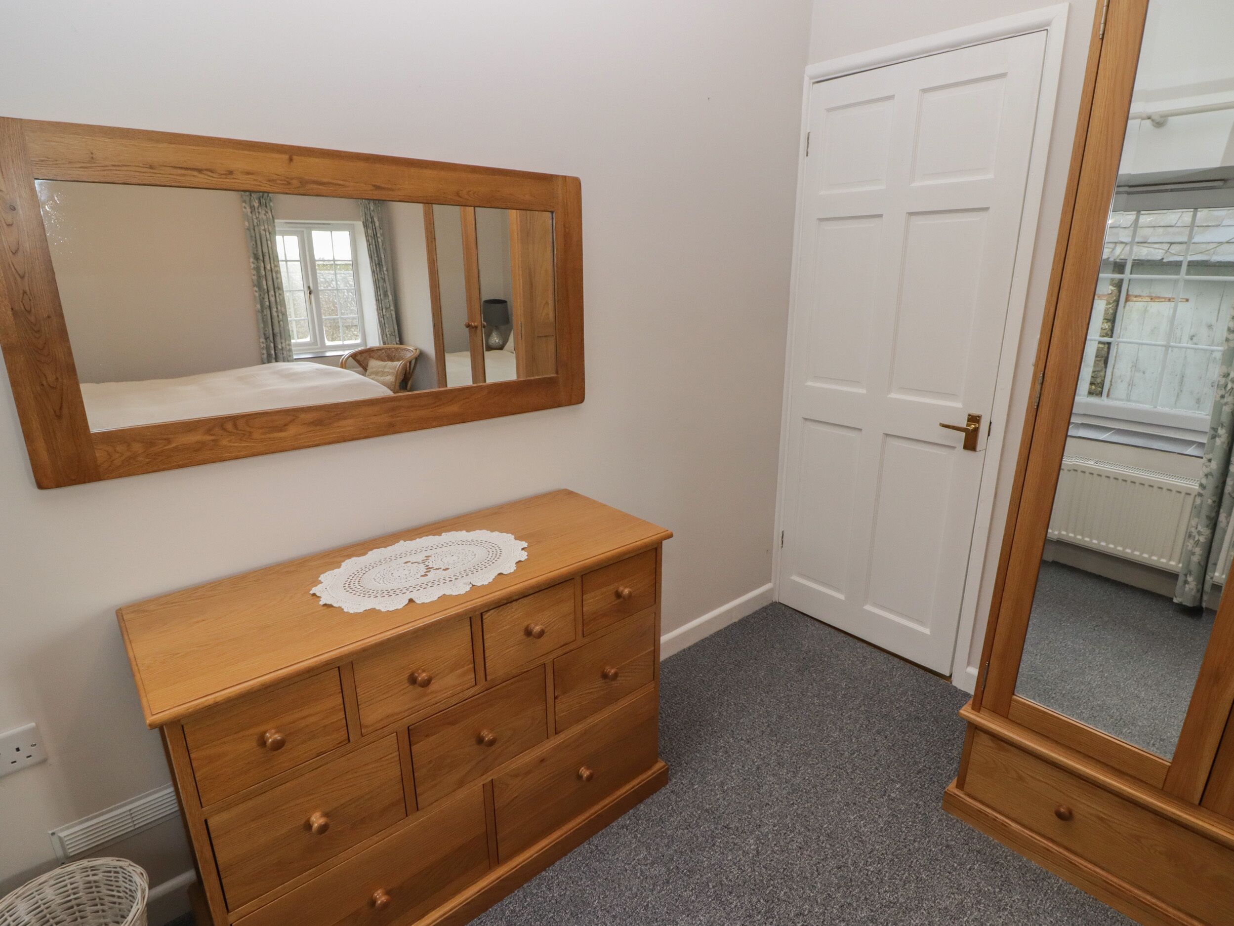 A bedroom with a wooden dresser, a large mirror, and a white door.