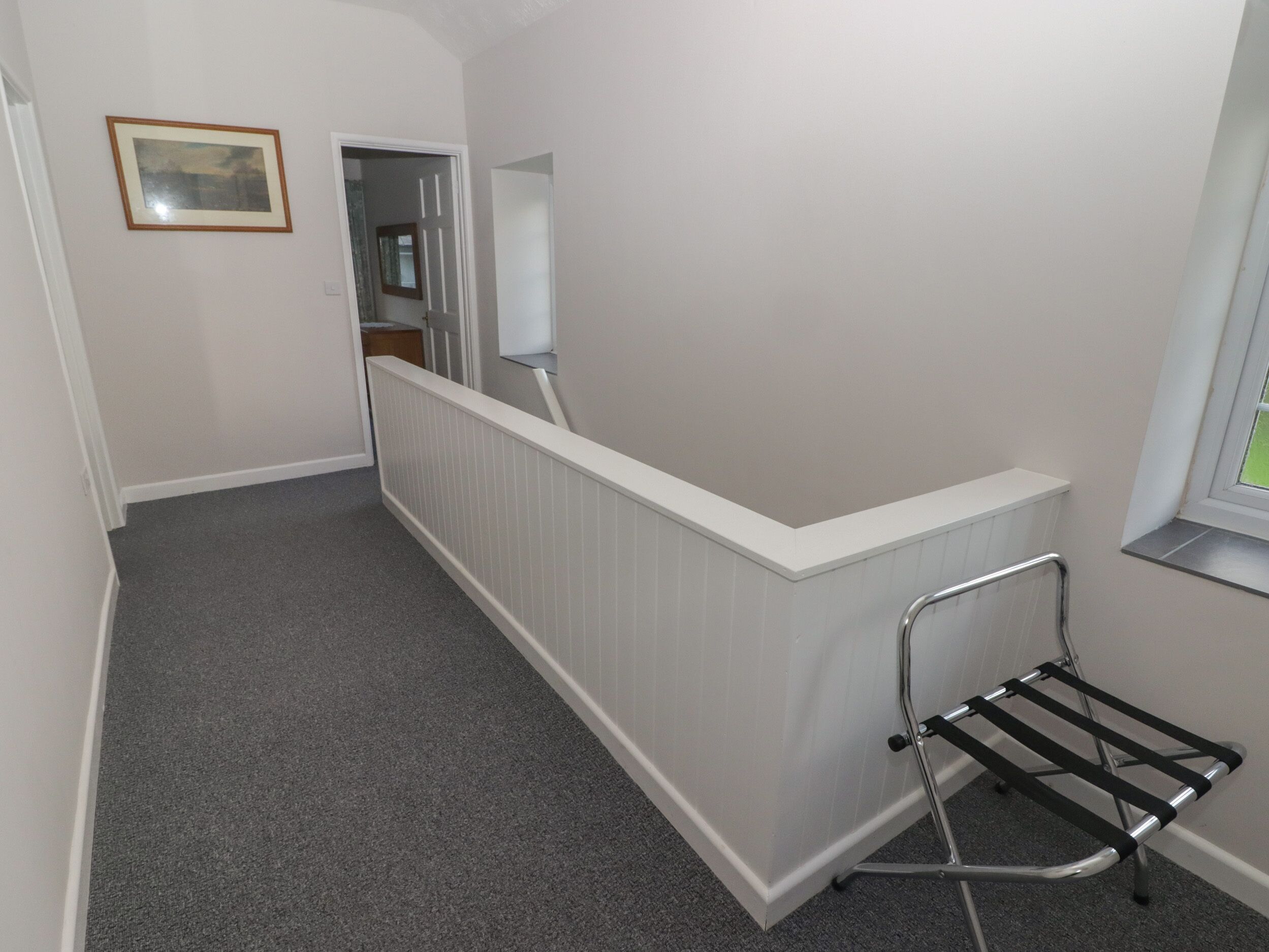 Un couloir étroit avec un radiateur, un étagère métallique et un tableau encadré accroché au mur.