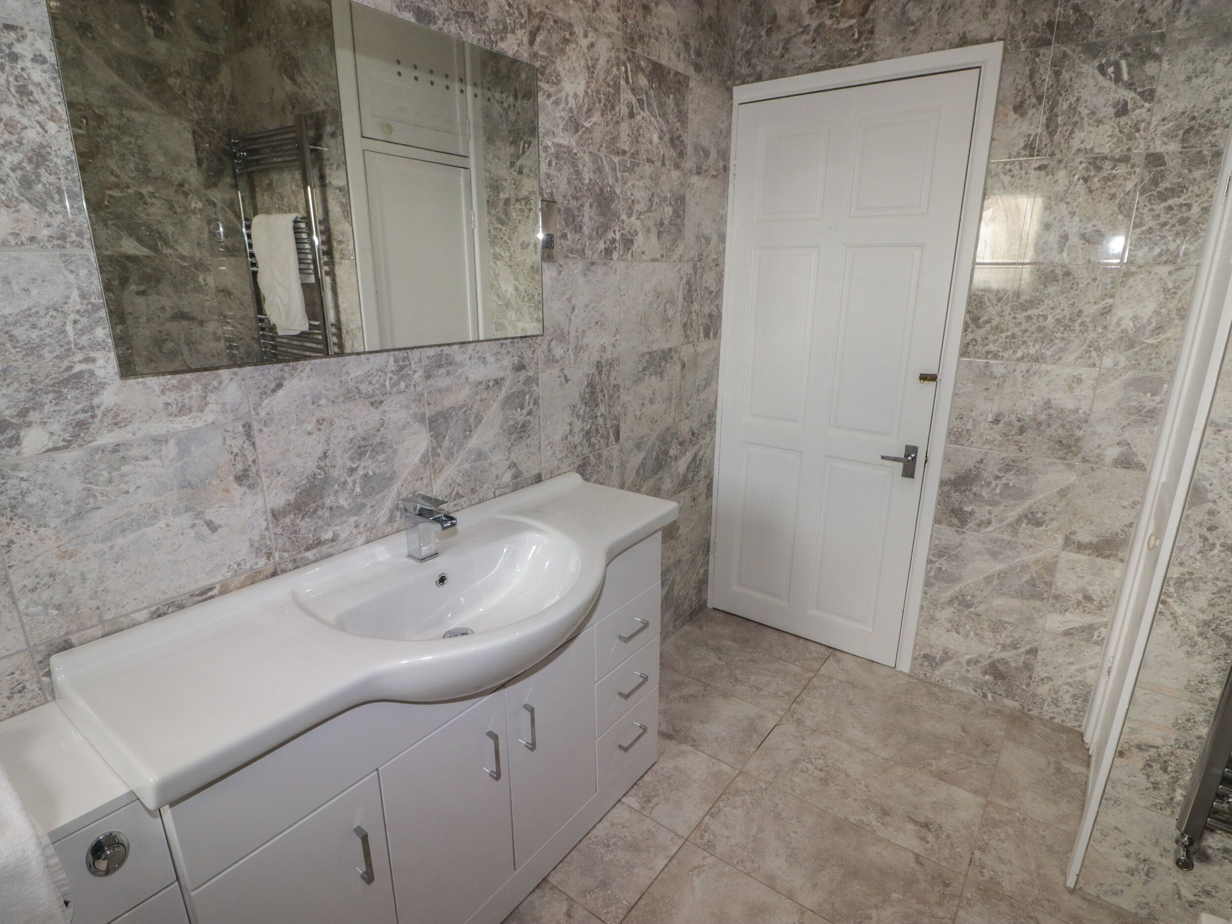 A bathroom with a white sink, marble walls, and a white door.