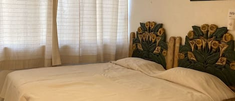 Ein Schlafzimmer mit zwei Betten, einer grünen Akzentwand, einem Fenster mit Vorhängen und einem gerahmten Blumenbild an der Wand.