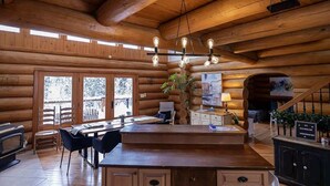 A log cabin interior with a wooden dining area, a central island with seating, and a staircase leading to an upper level. - Sainte-Lucie Luxury, Chalet with Hot Tub, River & Sauna! (Sainte-Lucie-des-Laurentides)