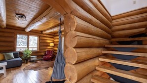 A log cabin interior with a wooden staircase, a hanging chair, and a sofa with cushions. - Sainte-Lucie Luxury, Chalet with Hot Tub, River & Sauna! (Sainte-Lucie-des-Laurentides)