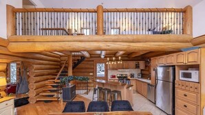 A log cabin interior with a dining area, kitchen, and a staircase leading to a loft. - Sainte-Lucie Luxury, Chalet with Hot Tub, River & Sauna! (Sainte-Lucie-des-Laurentides)