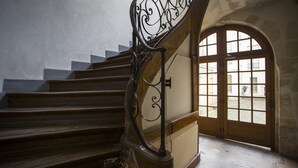 A staircase with a wrought iron railing and a wooden handrail, leading to a room with a large arched window. - Peaceful appartement in the heart of Le Marais  (Paris)