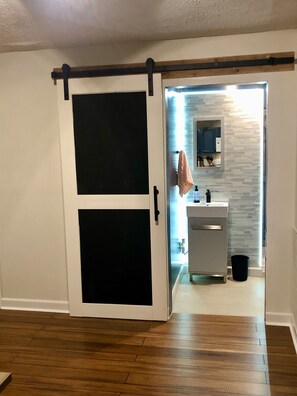 Une pièce dotée d’une porte coulissante donnant accès à une salle de bain avec un mur recouvert de carreaux et un lavabo.