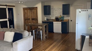 Una cocina moderna con suelo de madera, un comedor con taburetes y un refrigerador.