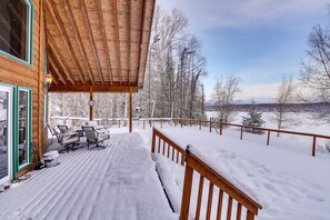 A wooden deck with outdoor seating and a view of snow-covered trees and mountains. - Wasilla 'Spruce Moose' Cabin: Lakefront + Hot Tub! (Wasilla)