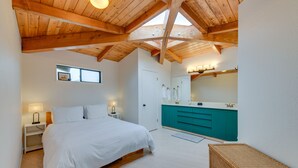 Un dormitorio con techo de madera, una cama, una mesita de noche, un espejo y un baño con armarios color turquesa.
