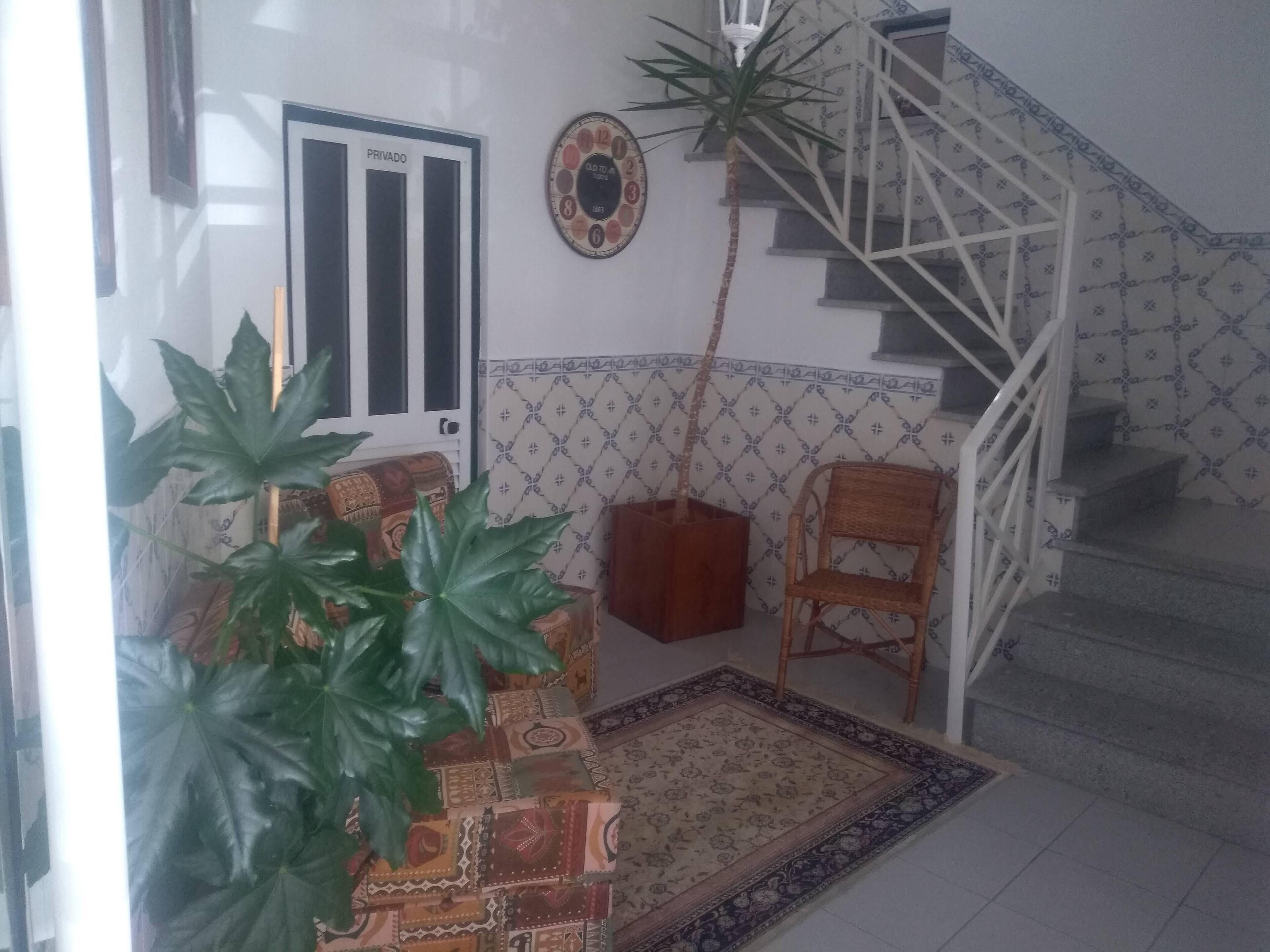 Una escalera con un papel tapiz estampado, una puerta con la leyenda 'PRIVADO', una planta en maceta y una silla de mimbre.