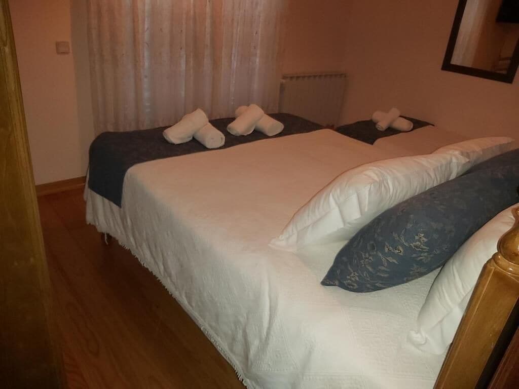 Camera d'albergo con due letti, ognuno con asciugamani ordinatamente piegati e un cuscino a motivi blu.