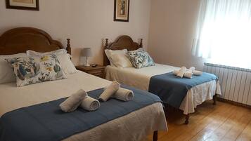 A hotel room with two beds, each with a wooden headboard, white linens, and blue bedspreads. There are two bedside tables with lamps and a framed picture on the wall.