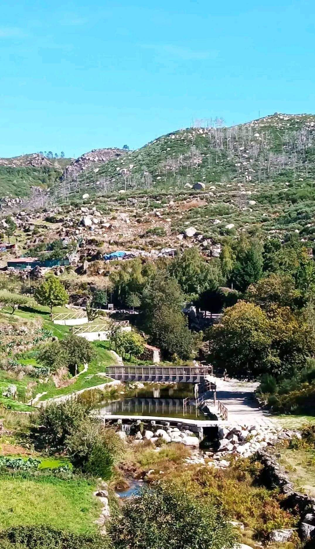 A mountainous landscape with a bridge, a pond, and scattered buildings.