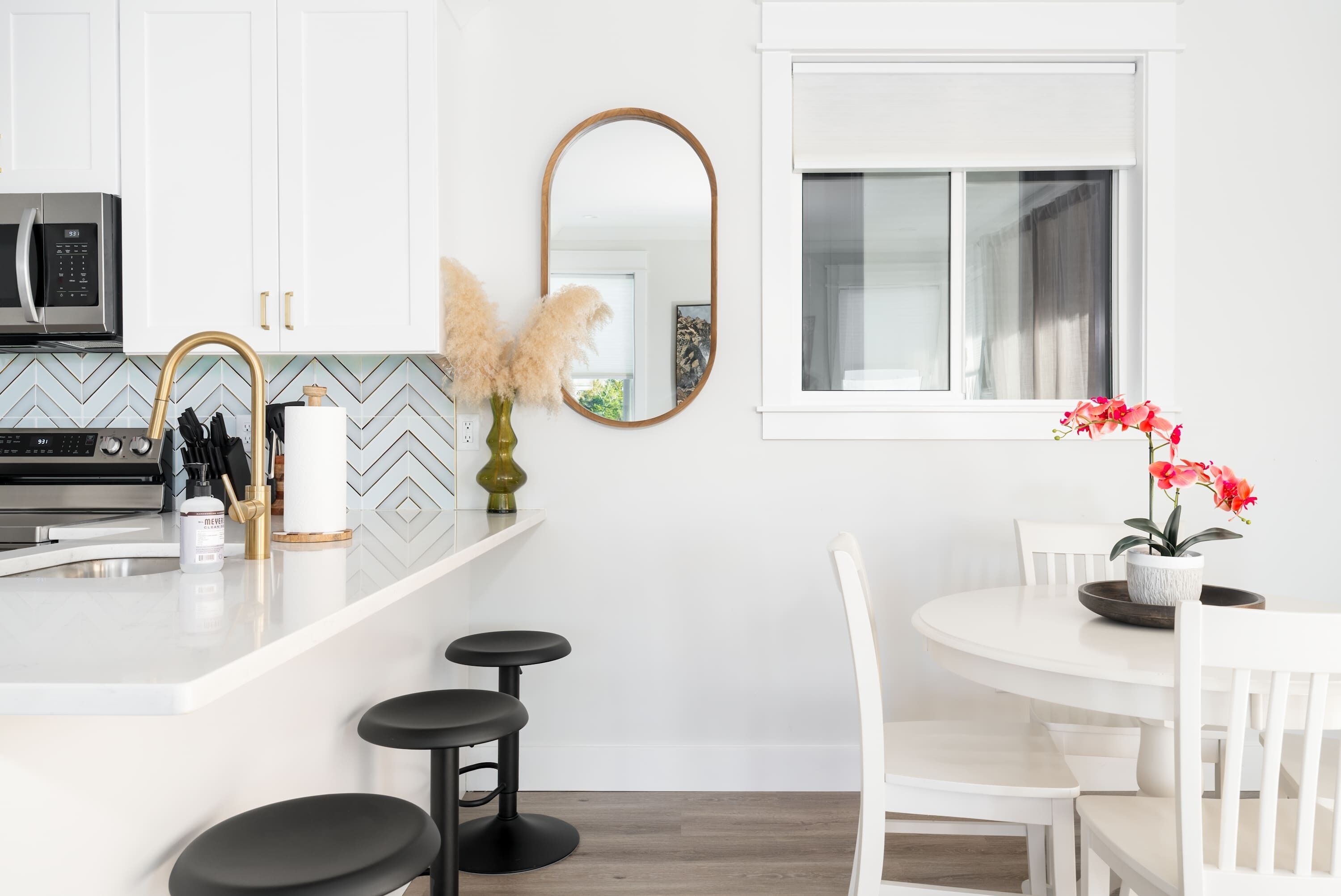 Een moderne keuken met witte kasten, een roestvrijstalen magnetron, een rond kookeiland met krukken en een eettafel met stoelen.
