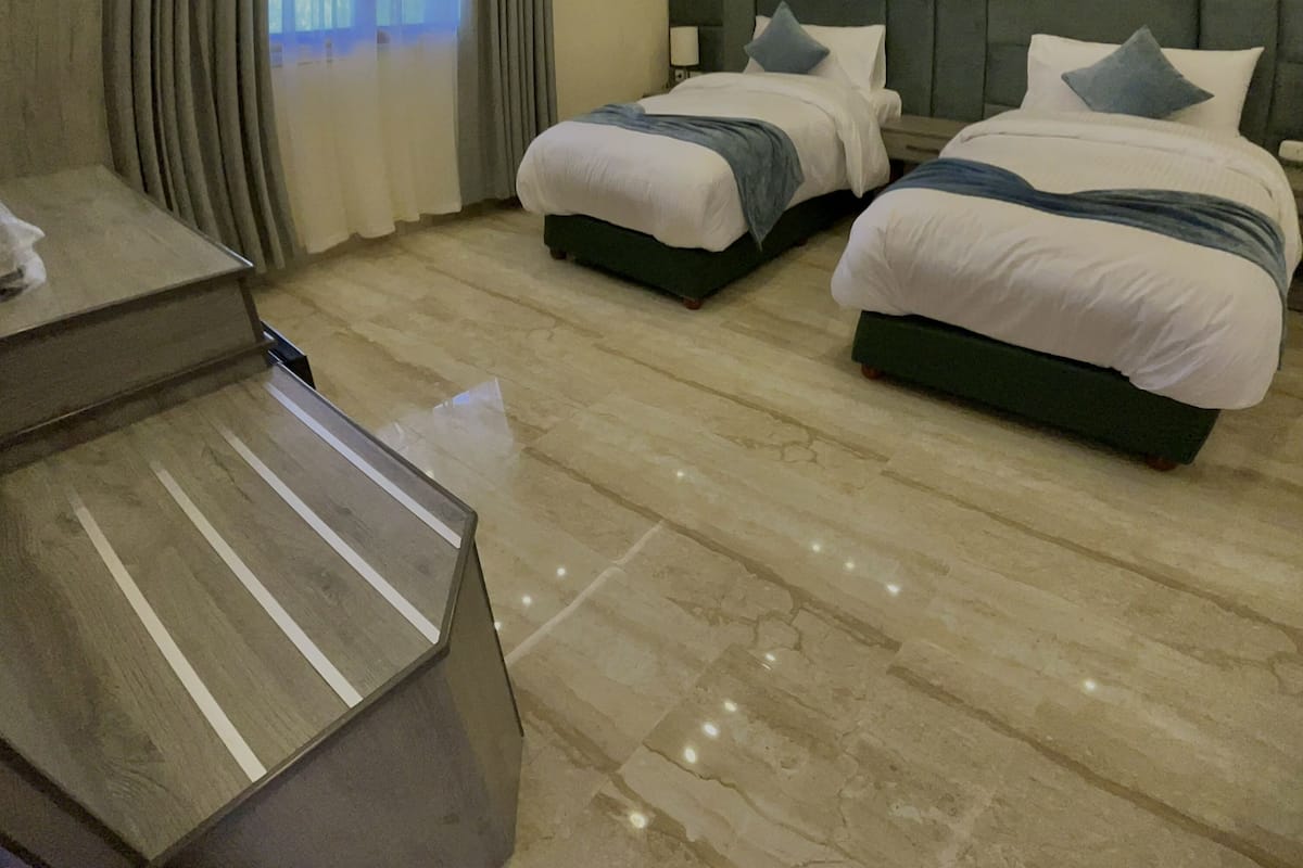 Quarto de hotel moderno com duas camas, uma escrivaninha e uma janela grande com cortinas.