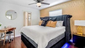 Un dormitorio con cama, escritorio, silla, ventilador de techo y mesita de noche con lámpara.
