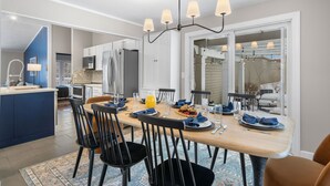 A modern kitchen with white cabinets, a central island, and a dining area with a wooden table and black chairs. - 3 Mins to ND. Hot Tub, Game Room, Sleeps 16, Fire Pit (South Bend)