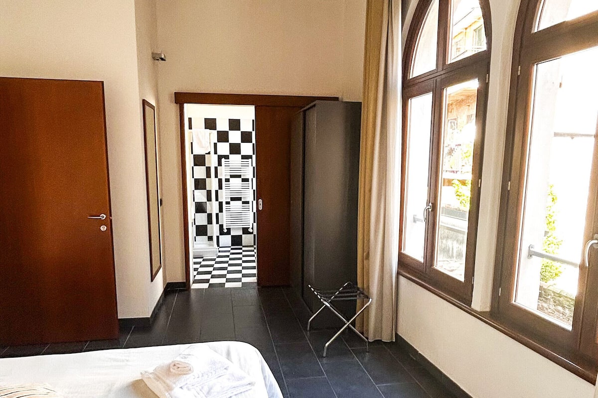 A hotel room with a bed, a checkered door, and large windows.
