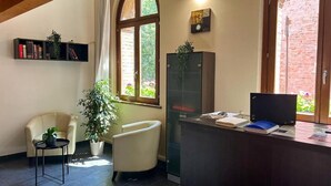 Zona de recepción con escritorio, una silla, estantería, planta en maceta y un ventanal grande.