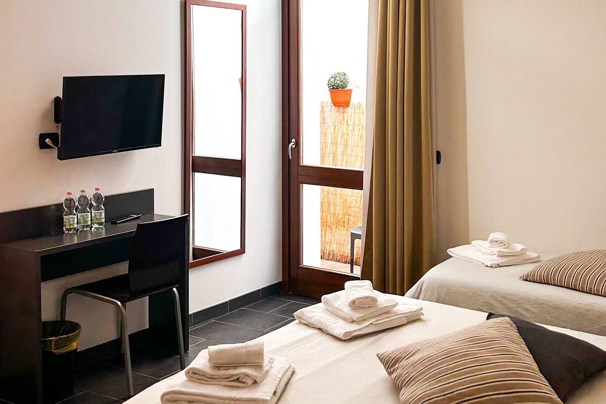 A hotel room with a bed, a desk, a television, and a window with curtains.