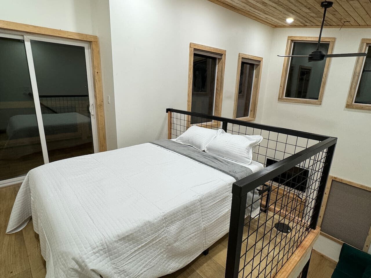 Une chambre à coucher avec un lit, une porte-fenêtre coulissante et un ventilateur de plafond.