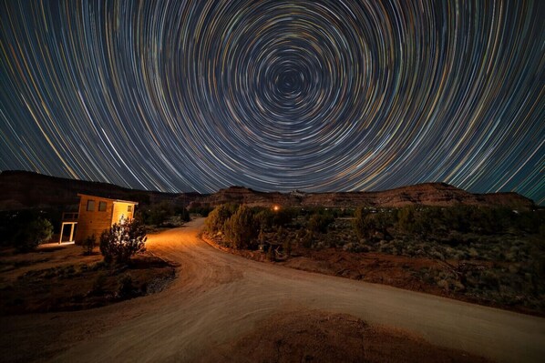 A star trail photograph of a desert landscape with a building and a dirt road.
