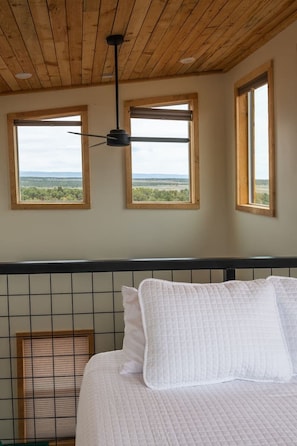 A bedroom with a bed, a ceiling fan, and three windows with views of the landscape. - Tiny Cabin, #6 8-Mile Gap View @ The Cedars (Kanab)