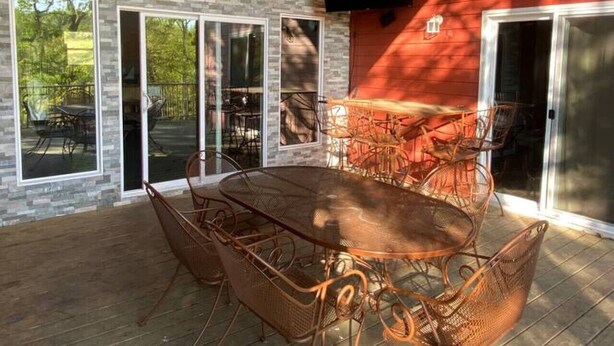 Eine Terrasse im Freien mit einer Steinsäule, einem großen Tisch mit Metallstühlen und einem roten Gebäude im Hintergrund.
