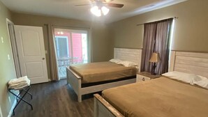 Ein Hotelzimmer mit zwei Betten, einem Deckenventilator, einer Tür, die auf einen Balkon führt, und einem kleinen Tisch mit einer Lampe.